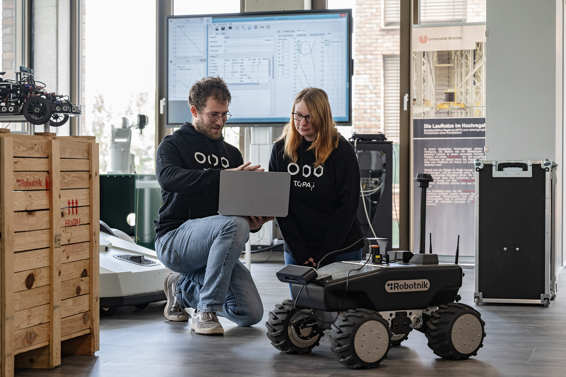 Eine Frau und ein Mann programmieren an einem Laptop einen Roboter