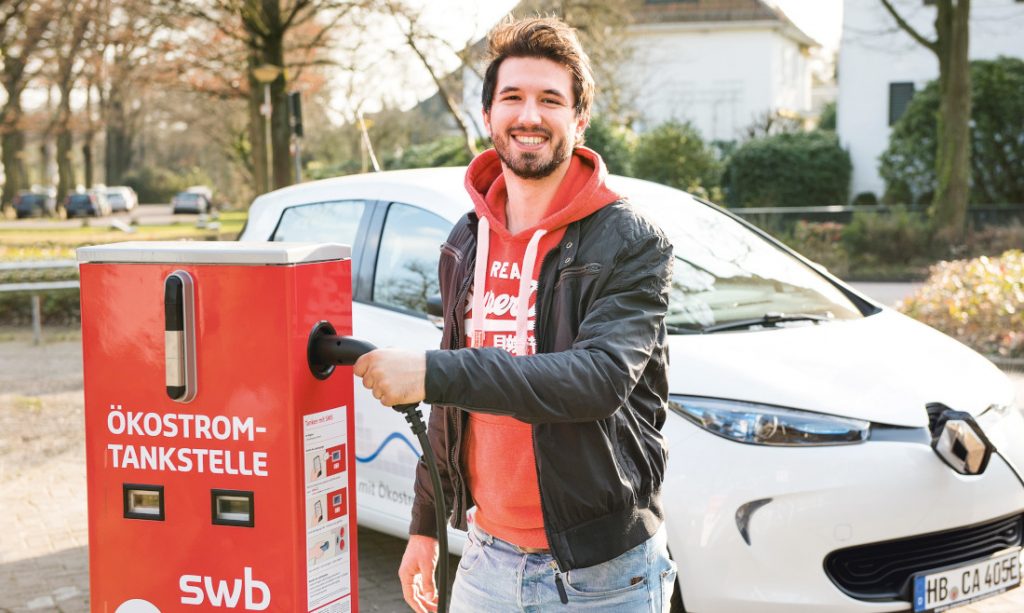 Ein Mann in rotem Kaputzenpullover und Lederjacke lädt sein Elektroauto an einer swb Ökostrom-Tankstelle