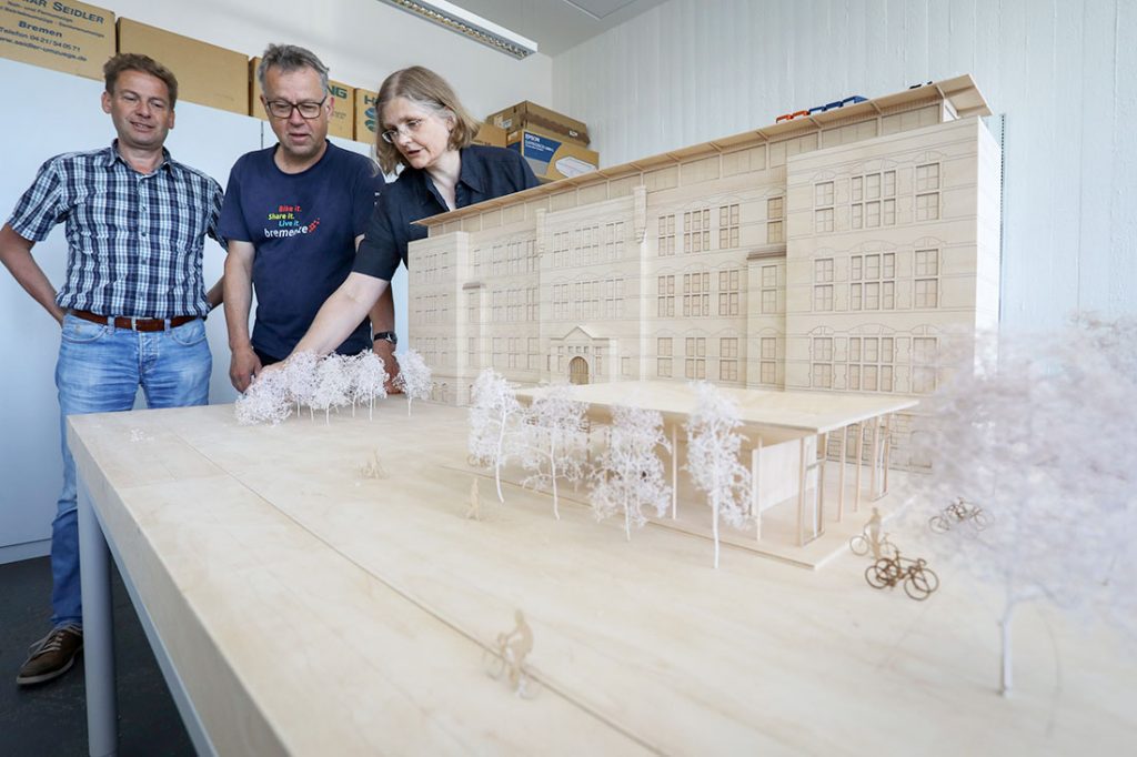 Zwei Männer und eine Frau stehen hinter einem Modell der Hochschule Bremen