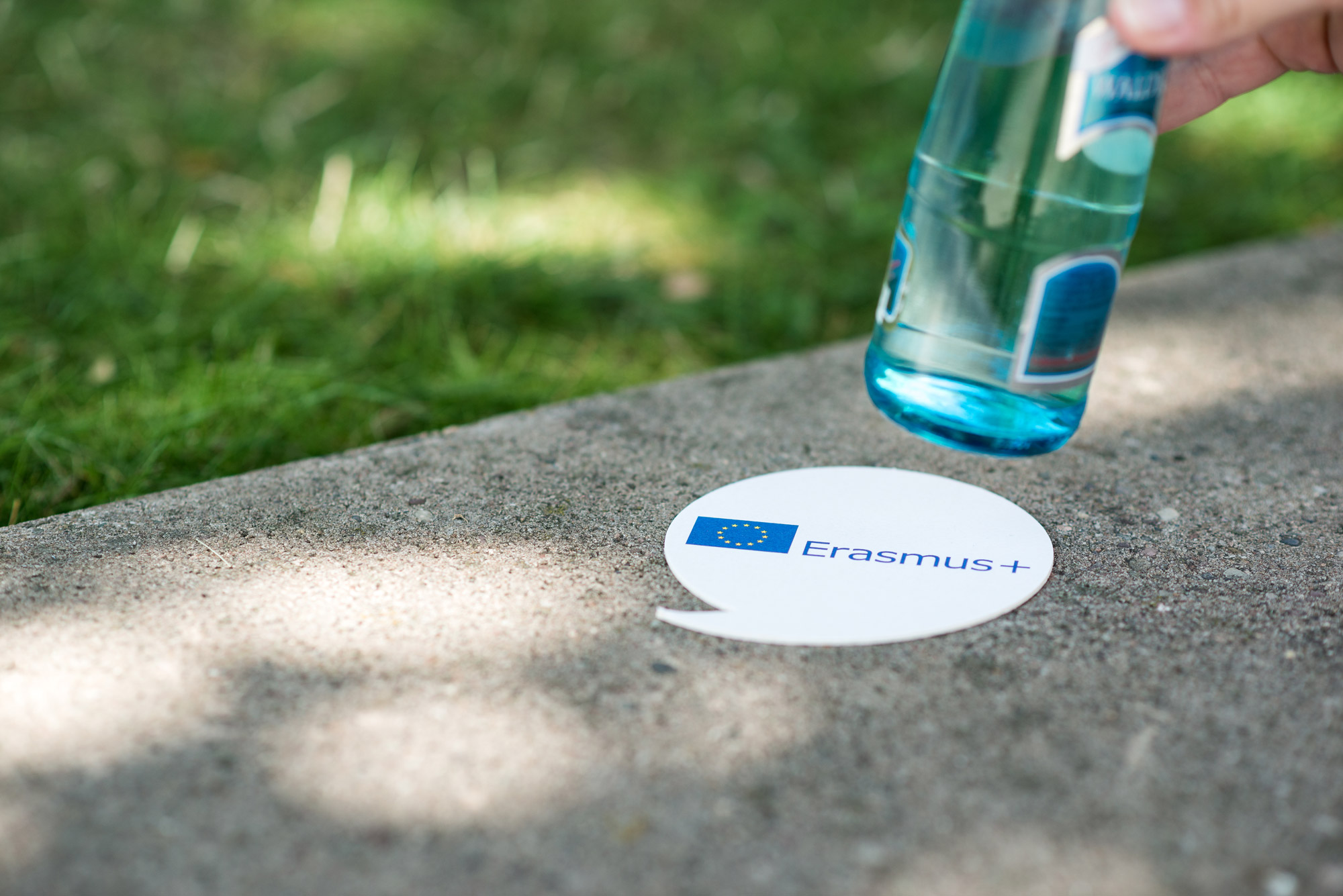 Ein Getränkeuntersetzer mit dem Erasmus + Logo, von dem eine Wasserflasche hochgehoben wird
