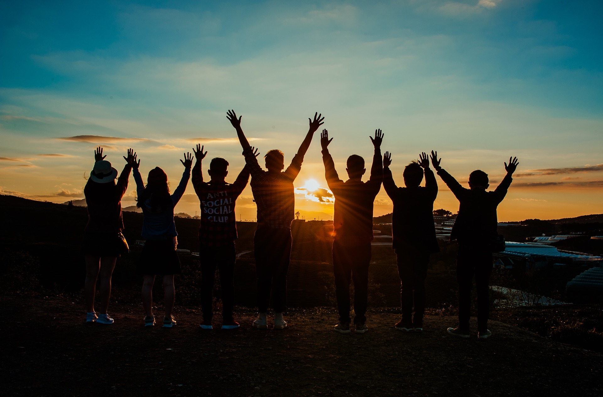 Eine Gruppe junger Menschen im Gegenlicht bei Sonnenuntergang, die die Hände nach oben streckt