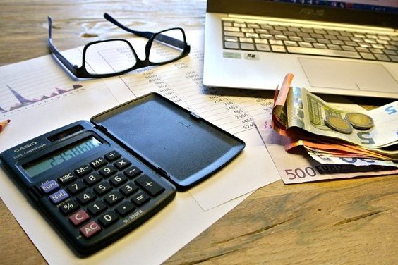 Ein Taschenrechner, eine Brille, Dokumente und Bargeld liegen auf einem Schreibtisch