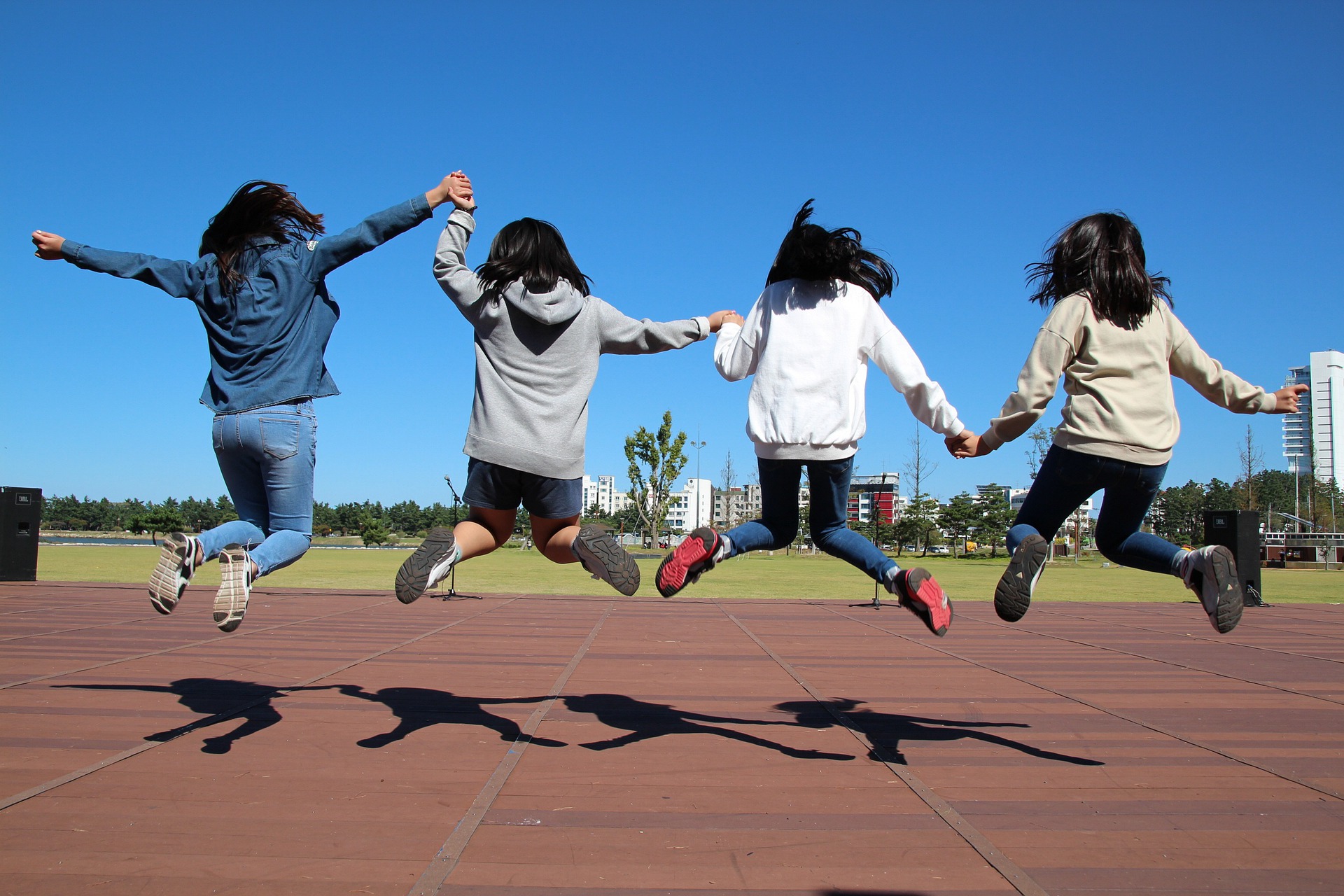 Vier junge Mädchen sind von hinten zu sehen, wie sie hochspringen und sich dabei an den Händen halten