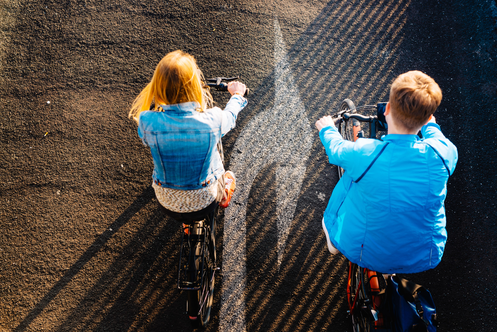 Ein Mann und eine Frau fahren Fahrrad. Das Foto ist eine Luftaufnahme. Am Boden ist ein Rechtsabbieger-Pfeil auf dem Asphalt zwischen den beiden Fahrrädern zu sehen.