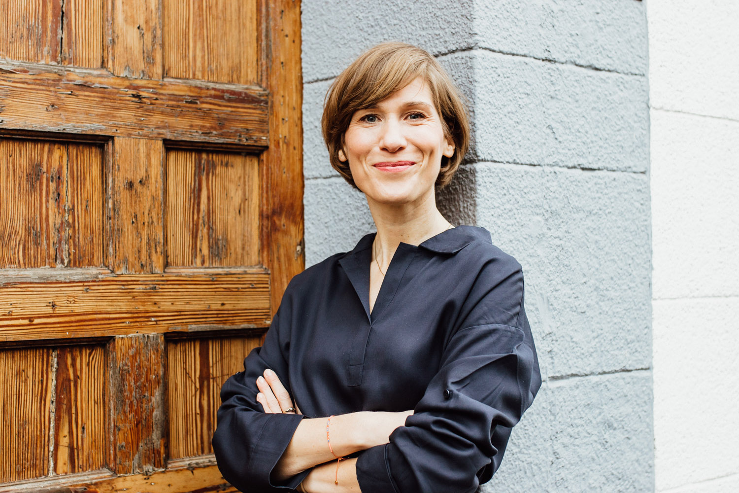 Eine Frau mit kürzeren Braunen Haaren die an einer Wand steht. Sie guckt stolz und glücklich in die Kamera. Ihr Name ist Sandra Lachmann.