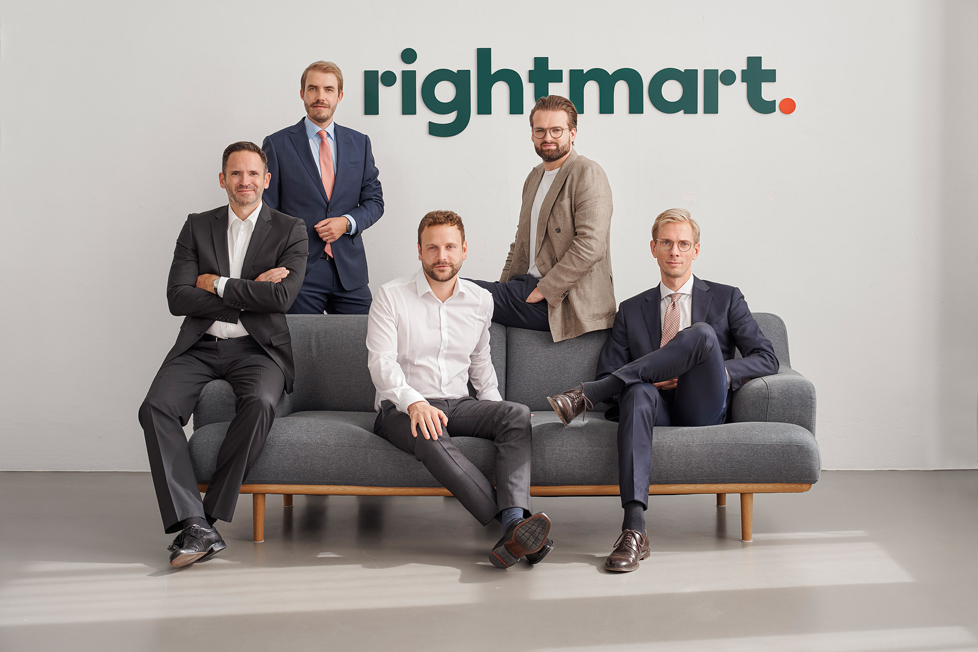 Fünf Männer in Anzügen sitzen auf einer Couch. Im Hintergrund ist das Logo von rightmart. zu sehen.