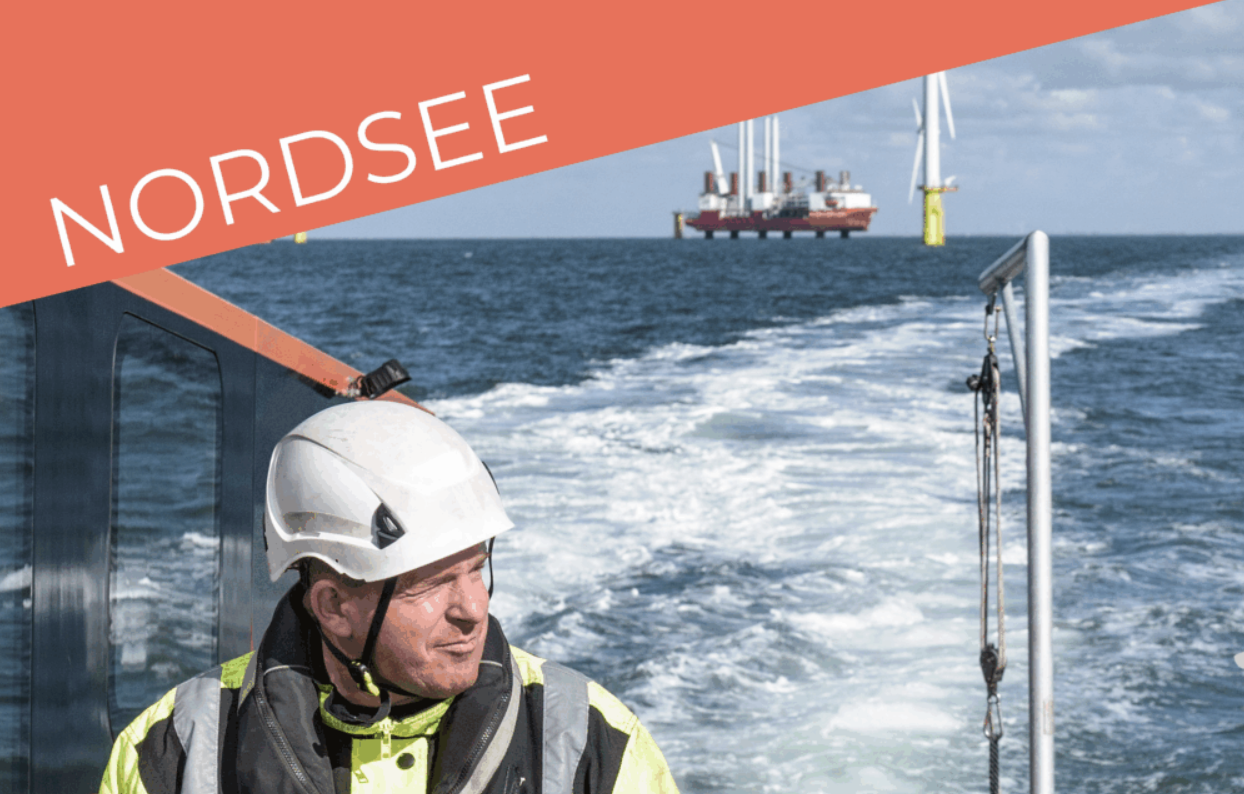 Ein Mann steht am Meer, im Hintergrund sind Windkraftanlagen und ein Schiff zu sehen